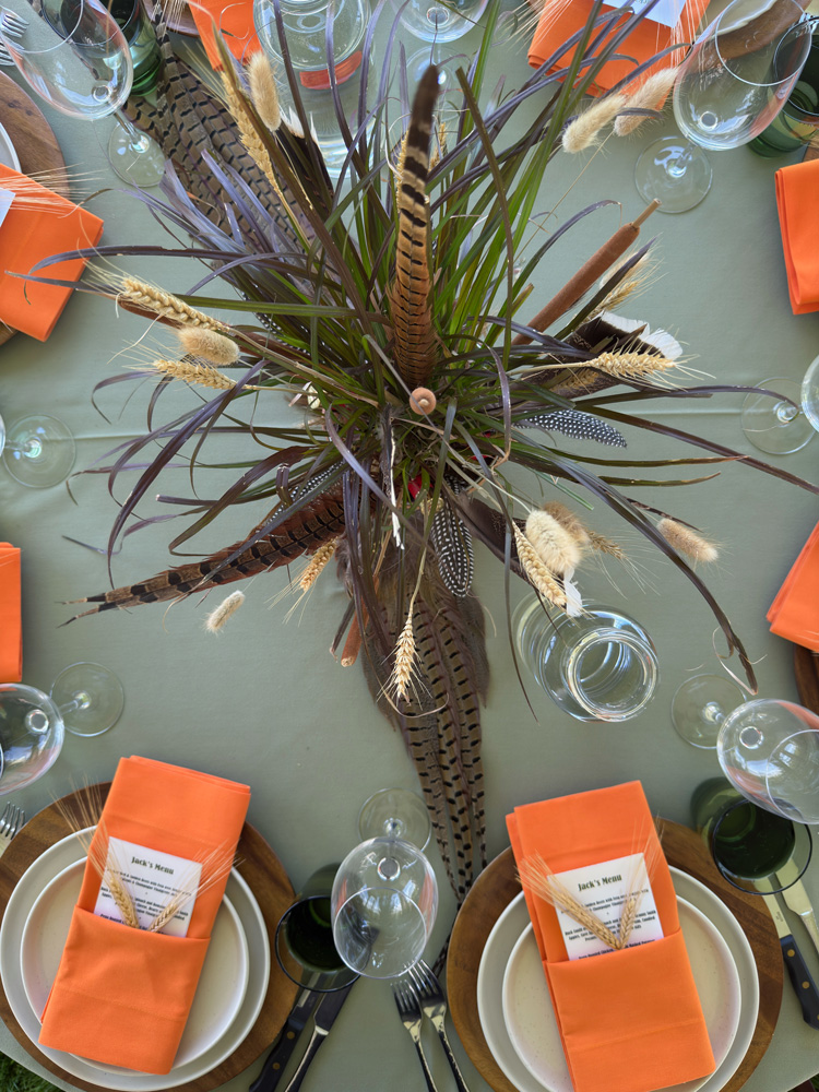 Table setting for Jack's 100 person birthday celebration meadow plants, feathers and wine glasses
